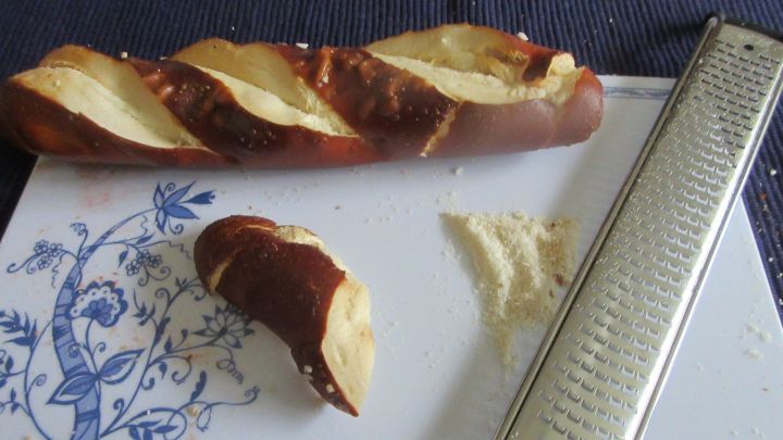 Ein Laugengeb&auml;ck liegt auf einem Teller, w&auml;hrend eine Reibe daneben steht, um Reste kreativ zu verwerten.