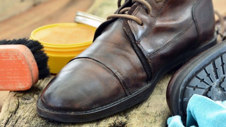 Braune Lederschuhe stehen auf einem Holzuntergrund, umgeben von Pflegematerialien wie B&uuml;rste, Creme und Tuch.