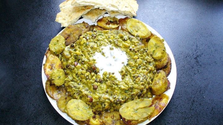 Ein Teller mit indischem Dal, umgeben von gebratenen Kochbananen und einem St&uuml;ck Fladenbrot, auf dunklem Hintergrund.