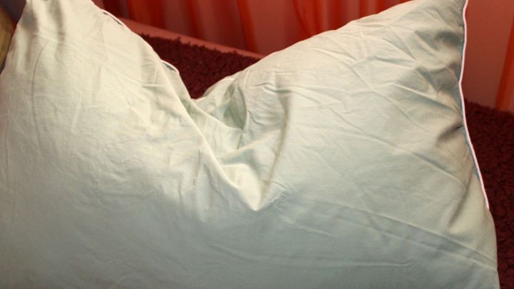 Eine zerknitterte Kissenh&uuml;lle liegt auf einem dunklen Untergrund, umgeben von orangefarbenem Stoff, was eine gem&uuml;tliche Atmosph&auml;re erzeugt.