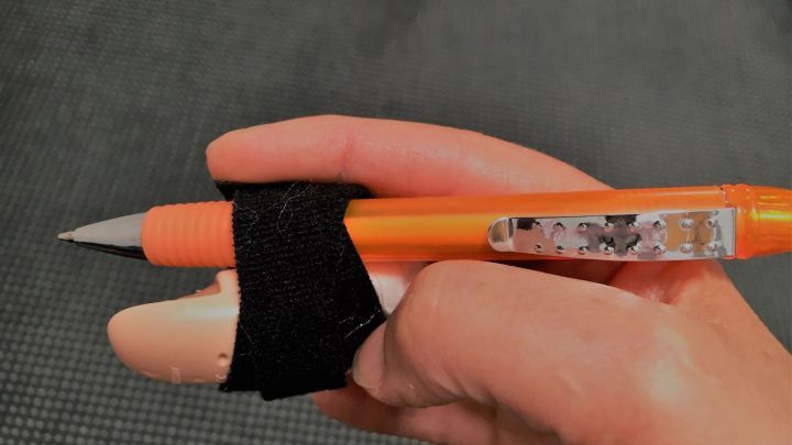 Eine Hand h&auml;lt einen Stift, w&auml;hrend die Fingerschiene das Schreiben nach einem Strecksehnenabriss unterst&uuml;tzt.