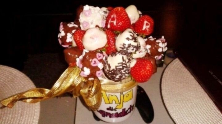 Ein bunter Erdbeer-Schoko-Strau&szlig;, der in einer Tasse arrangiert ist, gl&auml;nzt in einem dunklen Raum, umgeben von einer eleganten Tischdeko.