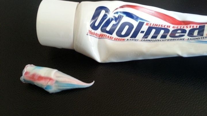 Eine Tube Zahncreme liegt auf einer dunklen Oberfl&auml;che, w&auml;hrend ein kleiner Klecks Zahnpasta daneben sichtbar ist.