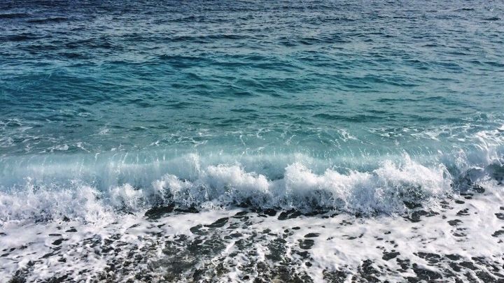 Sanfte Wellen rollen an einen Kiesstrand, w&auml;hrend das klare Wasser unter einem bew&ouml;lkten Himmel pl&auml;tschert.