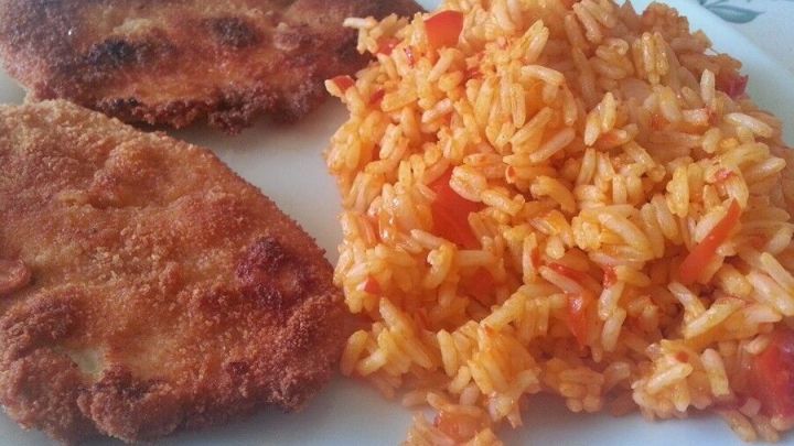 Ein Teller zeigt Djuvec-Reis, der mit gebratenem Fleisch serviert wird, auf einem dekorierten Tisch.