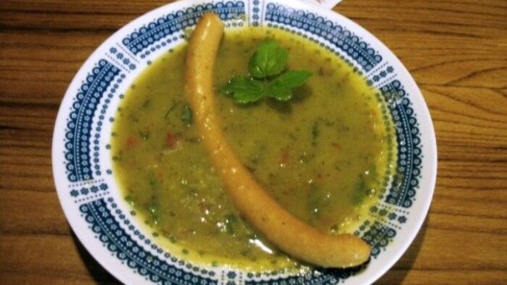 Eine bunte Gurken-Kartoffel-Suppe in einer sch&ouml;nen Sch&uuml;ssel, garniert mit einer Banane und frischem Koriander auf einem Holztisch.