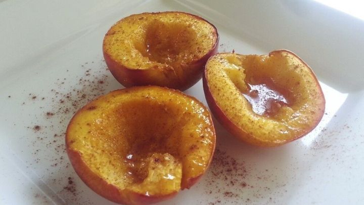 Gebackene Honig-Nektarinen liegen auf einem wei&szlig;en Teller, warm aus dem Ofen, best&auml;ubt mit Zimt.