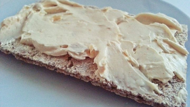 Ein Kn&auml;ckebrot mit cremigem Hummus und ger&ouml;stetem Knoblauch liegt auf einem wei&szlig;en Teller.