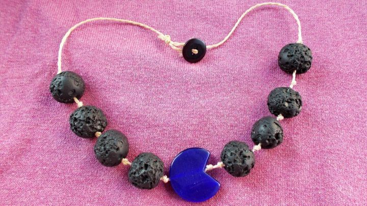 Ein sch&ouml;ner Lavastein-Halsreif aus FIMO in Herzform liegt auf einem lilafarbenen Tuch, umgeben von gleichfarbigen Perlen.