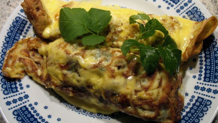 Zwei &uuml;berbackene Schinken-Spargel-Crepes liegen auf einem blauen Teller mit einem sch&ouml;nen Muster und sind mit Kr&auml;utern garniert.