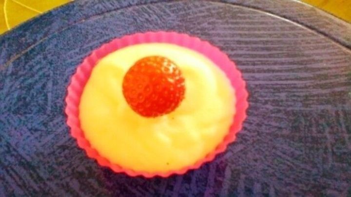 Ein Pudding-Eis in einer pinken Form, dekoriert mit einer Erdbeere, steht auf einem blauen Teller.