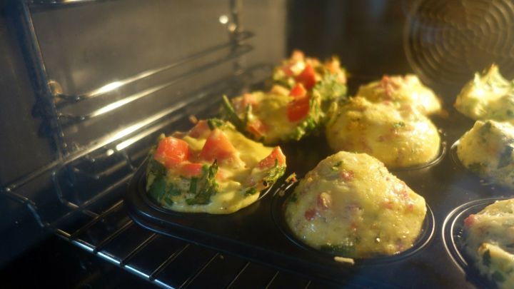 Omelette-Muffins backen im Ofen, leicht aufgebl&auml;ht mit Gem&uuml;se, pr&auml;sentieren sich in einer gl&auml;nzenden Backform.