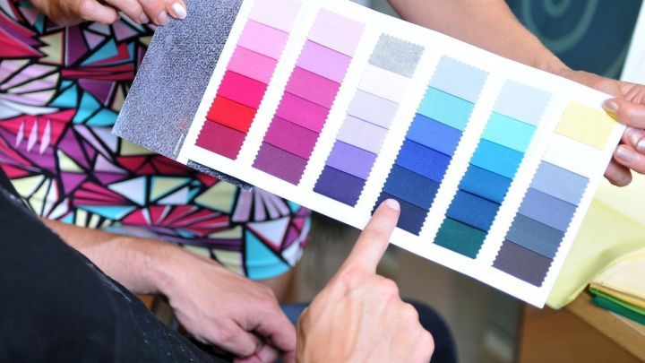 H&auml;nde halten einen Farbpass mit verschiedenen Farbt&ouml;nen, w&auml;hrend eine Person auf einen Farbton zeigt, um stilsicher einzukaufen.