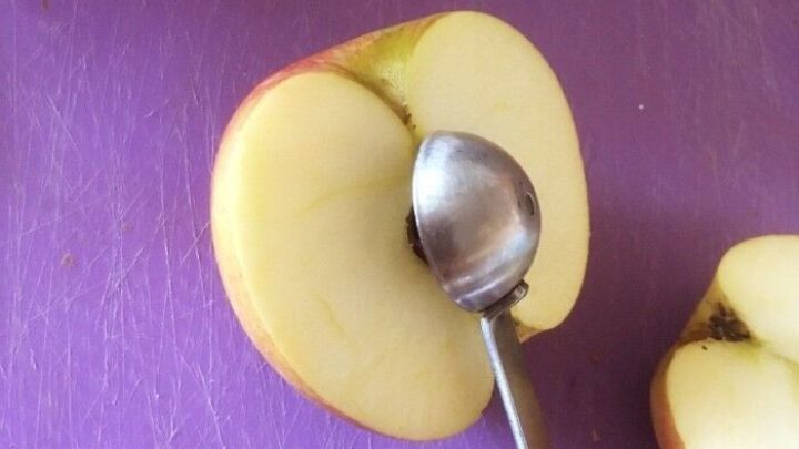 Ein halbierter Apfel liegt auf einer lila Schneidefl&auml;che, w&auml;hrend ein L&ouml;ffel das Kerngeh&auml;use schnell entfernt.