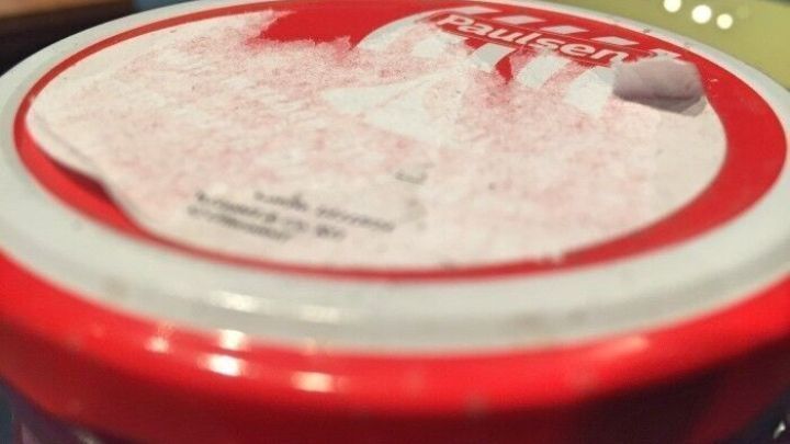 Ein Glasdeckel mit l&auml;stigen Kleberesten von einem Aufkleber, in einer bunten Umgebung sichtbar.