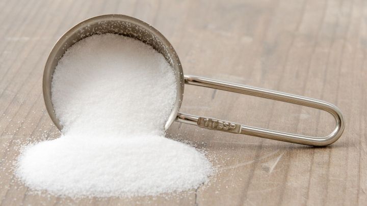 Ein Messbecher mit Zitronens&auml;ure steht auf einem Holztisch und gie&szlig;t Pulver, ideal zum Entkalken.