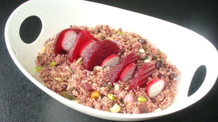 Ein Quinoasalat mit auff&auml;lligen roten Bete-Scheiben liegt dekorativ in einer wei&szlig;en Sch&uuml;ssel auf einem dunklen Untergrund.