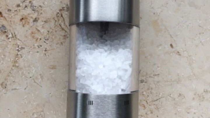 Ein silberner Salzstreuer aus Edelstahl steht auf einer hellen, marmorierten Oberfl&auml;che und enth&auml;lt grobes Salz.