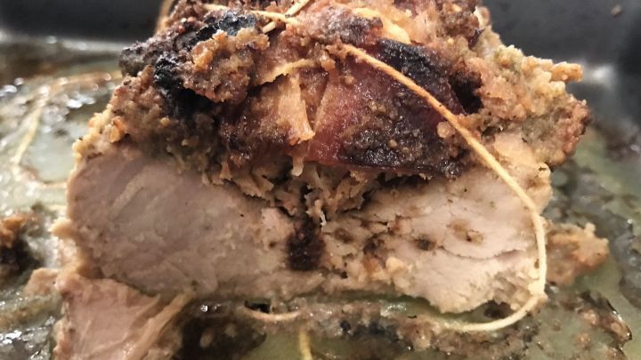 Gebackenes Schweinefilet mit einer knusprigen, gef&uuml;llten Kruste wird in einer Backform pr&auml;sentiert, umgeben von Bratensaft.