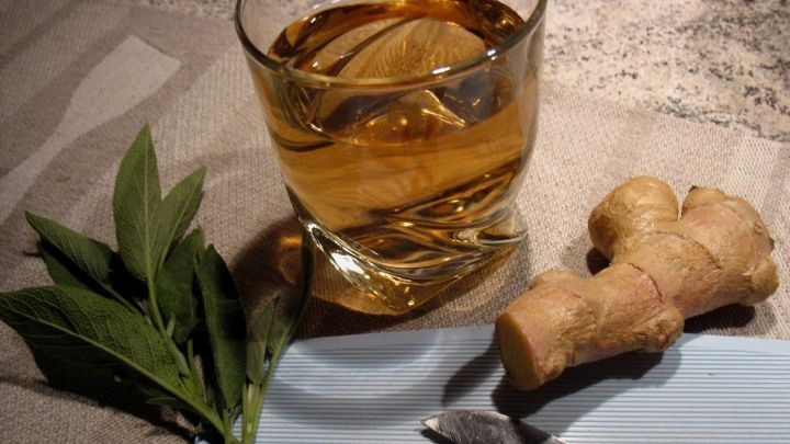 Ein Glas Salbei-Ingwer-Tee steht neben frischem Ingwer und geschnittenen Ingwerst&uuml;cken auf einem Holzschneidebrett.