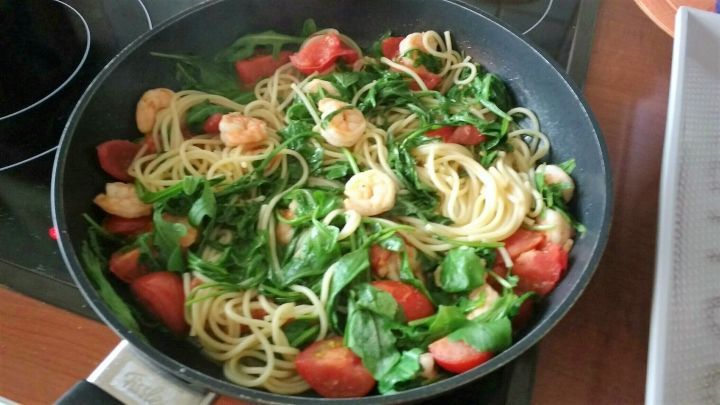 Frische Pasta mit Tomaten und Rucola wird in einer Pfanne zubereitet, umgeben von den Zutaten und einem modernen Kochfeld.