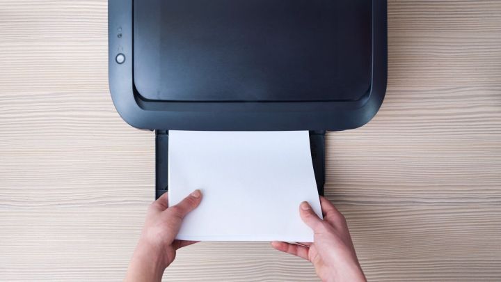 Ein Drucker wird verwendet, um ein Blatt Papier einzuziehen, w&auml;hrend H&auml;nde es an die Vorderseite halten.