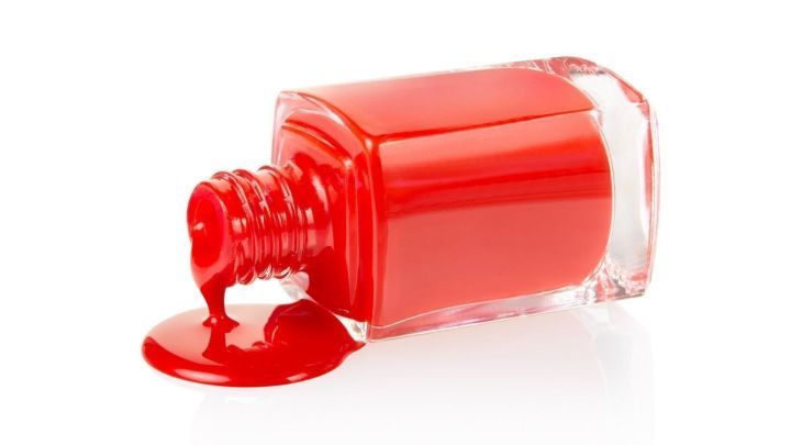 Ein roter Nagellack steht gekippt auf einem Tisch, w&auml;hrend er aus der Flasche l&auml;uft und eine Pf&uuml;tze bildet.