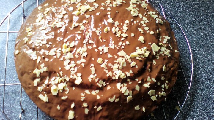 Ein Nusskuchen mit einer gl&auml;nzenden, schokoladigen Glasur und gehobelten N&uuml;ssen auf der Oberfl&auml;che steht auf einem Gitter.