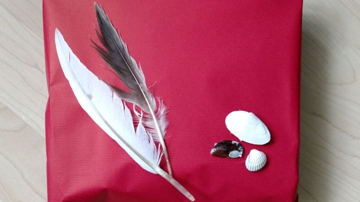 Ein sch&ouml;n verpacktes Urlaubs-Mitbringsel in rotem Geschenkpapier mit einer Feder und Kieselsteinen als Dekoration.