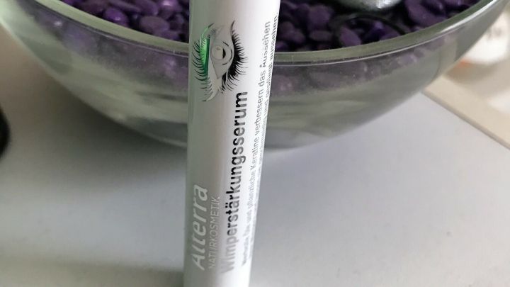 Ein Wimpernst&auml;rkungsserum steht auf einem Tisch, umgeben von lila Dekorsteinen und silbernen Dekorationen.