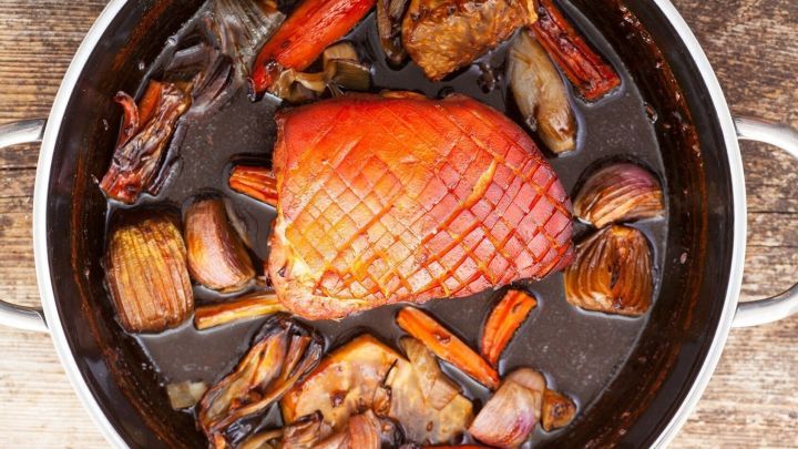 Ein St&uuml;ck geschmorter Schweinebauch liegt in einer Chilisauce mit Gem&uuml;se in einem Topf auf einer Holzoberfl&auml;che.