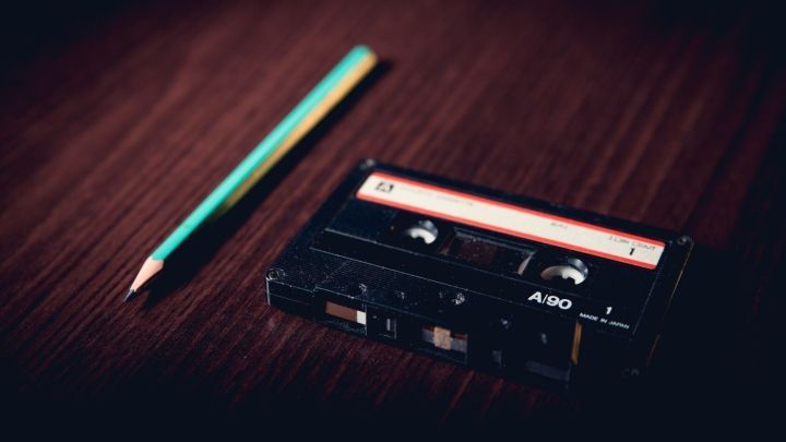 Eine Kassette liegt auf einem Holztisch neben einem gr&uuml;nen Bleistift, was Erinnerungen an aussterbende Sachen weckt.