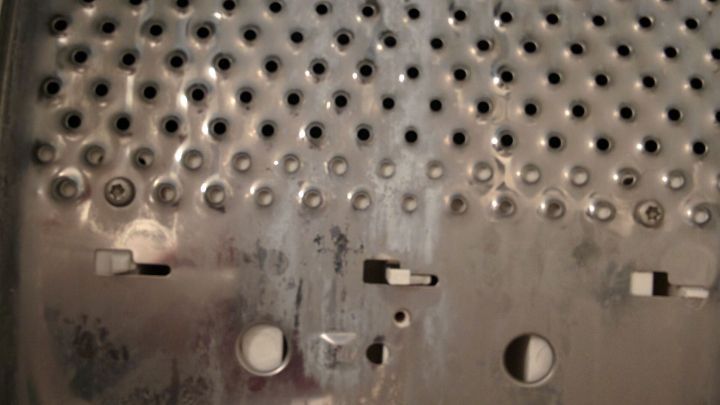 Der Hauptfokus liegt auf der Metalltrommel einer Waschmaschine, die Kalkablagerungen zeigt, und verdeutlicht den Entkalkungsprozess.