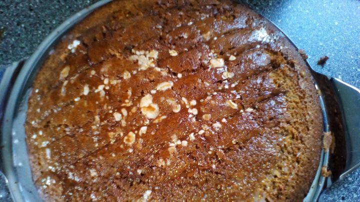 Ein goldbrauner Sprudelkuchen liegt auf einem klaren Kuchenmesser, umgeben von einer dunklen, glatten Arbeitsplatte.