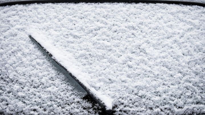 Eine Wischerd&uuml;se liegt auf einer mit Schnee bedeckten Windschutzscheibe, die vor Frost gesch&uuml;tzt werden muss.