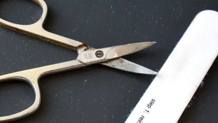 Eine abgenutzte Nagelschere liegt auf einer dunklen Unterlage neben einer Nagelfeile, bereit zur Reinigung.