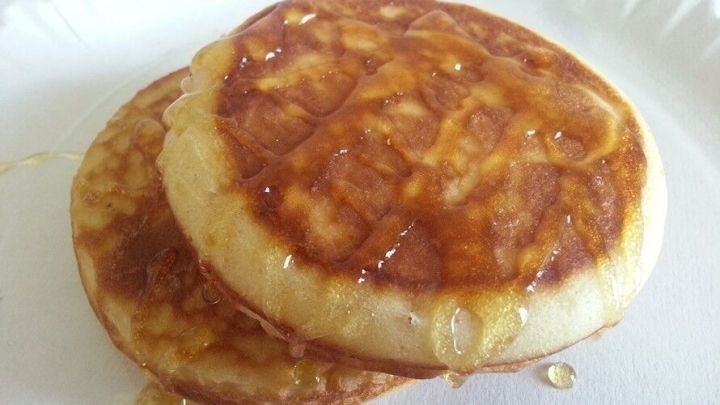 Zwei goldbraune Pancakes liegen auf einem wei&szlig;en Teller, leicht gl&auml;nzend mit Honig &uuml;berzogen, in einer gem&uuml;tlichen Umgebung.