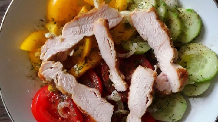 Ein Teller mit gesunden Zutaten wie Tomaten, Gurken und H&auml;hnchenbruststreifen, frisch zubereitet und appetitlich angerichtet.