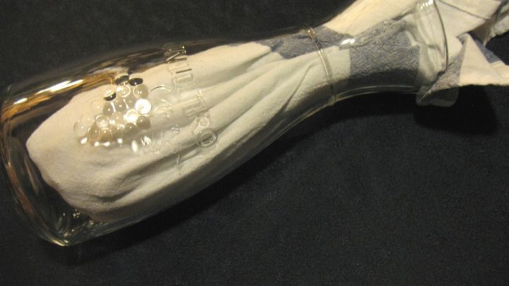 Eine Glaskaraffe mit einem Tuch darin, befindet sich auf einem dunklen Untergrund und trocknet nach dem Sp&uuml;len.