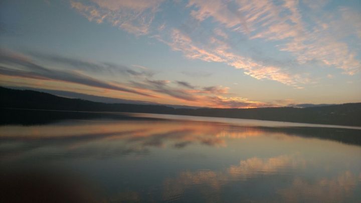 Sanfter Sonnenuntergang &uuml;ber einem ruhigen See, Reflexionen im Wasser schaffen eine friedliche, ber&uuml;hrende Atmosph&auml;re.