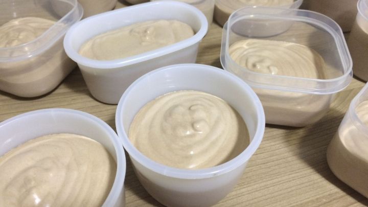 In mehreren transparenten Beh&auml;ltern ruht cremiges Schokoeis, das auf einem Holztablett f&uuml;r die K&uuml;hlung bereitsteht.