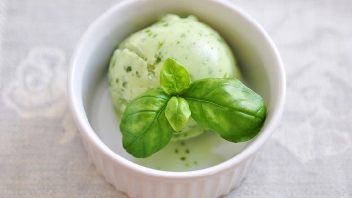 Gr&uuml;nes Basilikum-Eis in einer wei&szlig;en Sch&uuml;ssel, garniert mit frischem Basilikumblatt, auf einer zarten Tischdecke.