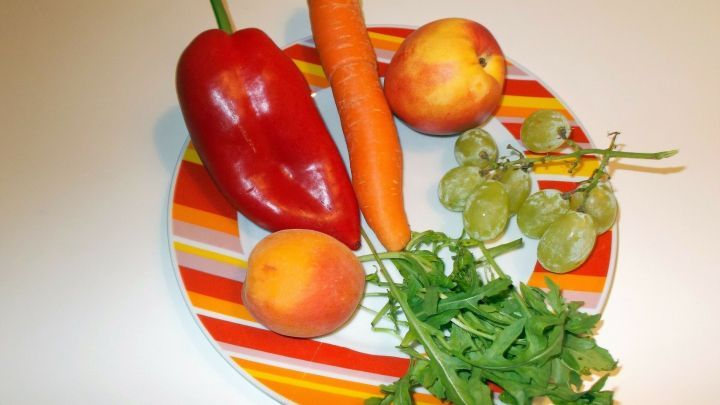 Auf einem bunten Teller liegen frisches Gem&uuml;se und Obst: Paprika, Karotte, &Auml;pfel und Rucola, bereit zum gesunden Essen.