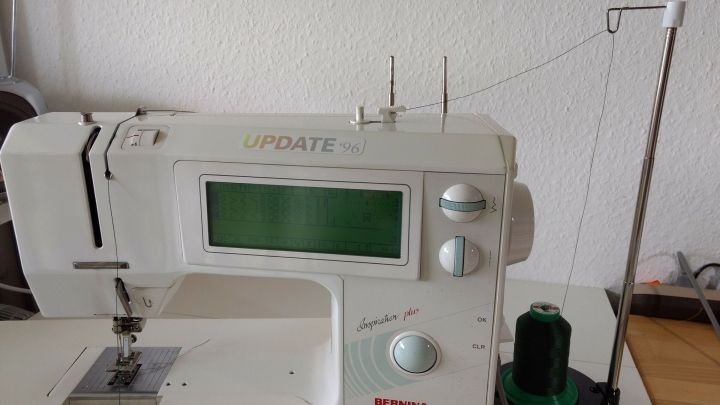 Eine N&auml;hmaschine mit Garnrollenhalter, der waagerecht positioniert ist, steht auf einem Tisch in einem hellen Raum.