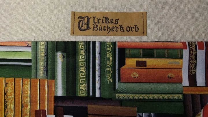 Ein B&uuml;cherregal aus verschiedenen bunten B&uuml;cher in antikem Stil. Oben ist ein Label mit mittelalterlicher Schrift, das "W&uuml;rzburger B&uuml;cherkorb" zeigt.