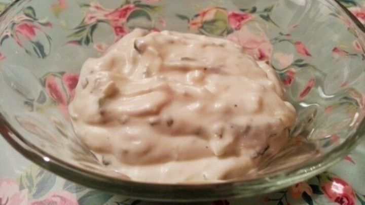 Eine Sch&uuml;ssel mit Zaziki steht auf einem blumigen Tisch. Die cremige Mischung sieht frisch und einladend aus.