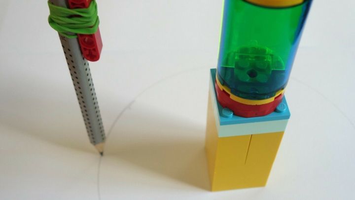 Ein Notzirkel aus Lego steht auf Papier und zeichnet einen Kreis, w&auml;hrend ein Stift in der Mitte fixiert ist.