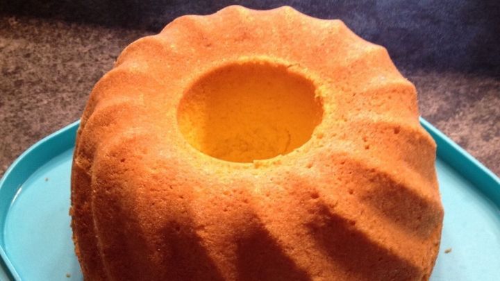 Ein Zitronengugelhupf steht auf einem blauen Teller und wartet darauf, serviert zu werden. Der Kuchen hat eine goldene Farbe.