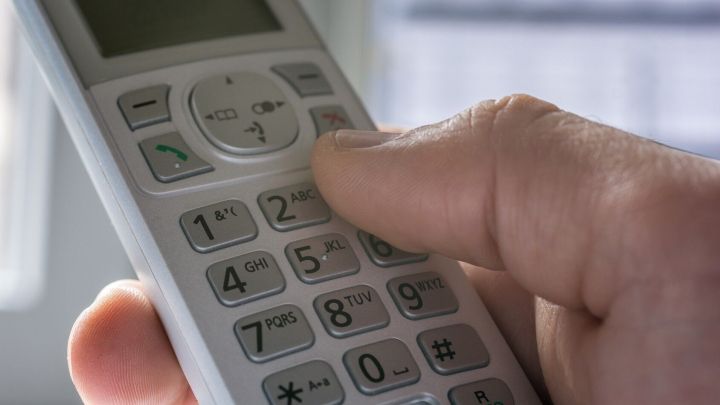 Ein Hand nutzt eine Telefontastatur, um eine Nummer einzutippen, w&auml;hrend Licht durch ein Fenster f&auml;llt.