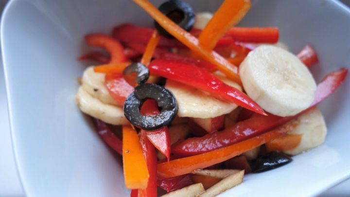 Bunte Paprika- und Bananenscheiben sowie Oliven sind in einer wei&szlig;en Sch&uuml;ssel angeordnet, frisch zubereitet f&uuml;r einen Salat.